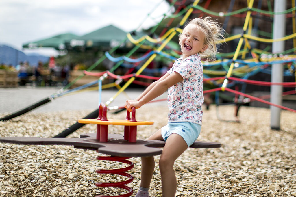 Ein Mädchen sitz auf einer Wippe am Spielplatz und lacht fröhlich